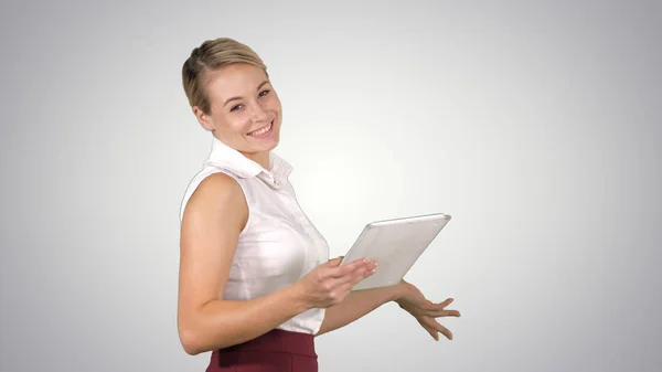 Female office clerk walking with tablet and smiling broadly when talking to camera on gradient background. — Stock Photo, Image