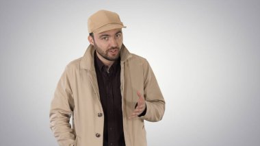 Bir trençkot yürüyüş ve degrade arka plan üzerinde konuşurken olumlu bir sakallı erkek giymiş.