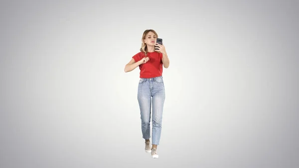 Bionda che cammina e si pavoneggia guardando al telefono su sfondo sfumato. — Foto Stock