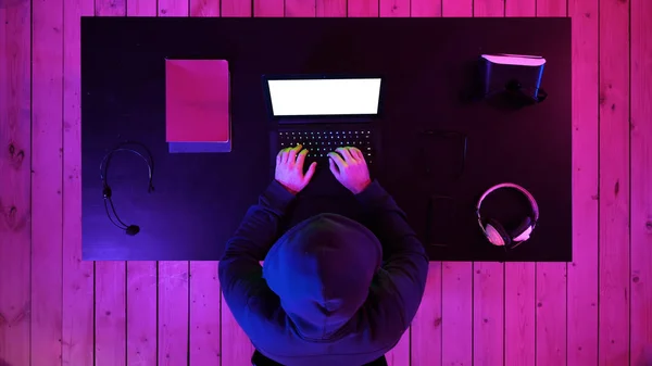 Hacker in hoodie typing code in program using laptop in dark studio. White Display.