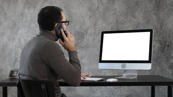 Un uomo che parla al telefono in ufficio e guarda sullo schermo del computer. Display bianco. — Foto Stock