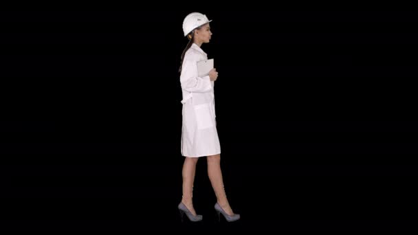 在阿尔法 全长侧视图 迷人的西班牙女人穿着白色实验室外套 头戴白色安全帽 手持笔记本电脑或平板电脑行走 阿尔法通道 专业拍摄4K分辨率 013 — 图库视频影像