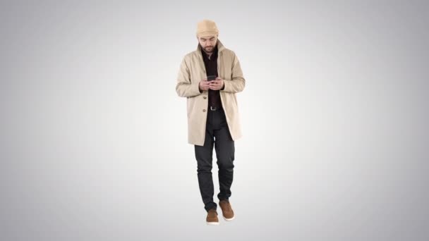Hombre guapo en camina capa y mensaje de texto en el teléfono en el fondo gradiente . — Vídeo de stock