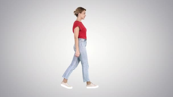 Mujer en camiseta roja, jeans y zapatillas de deporte caminando sobre fondo degradado . — Vídeo de stock