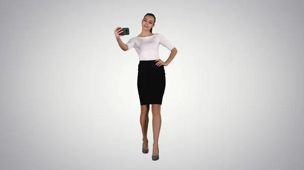 Mujer atractiva sonriente tomando una selfie mientras camina sobre fondo degradado . —  Fotos de Stock