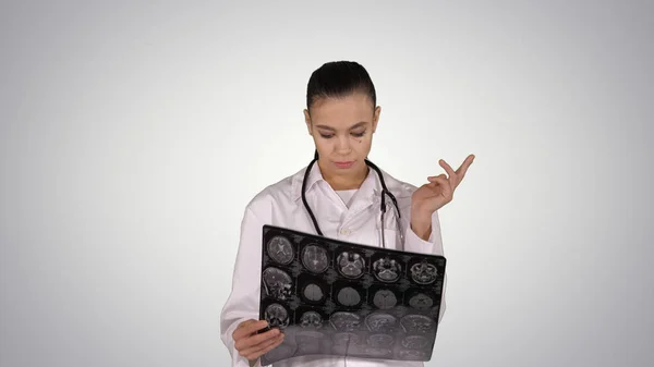 Γιατρός γυναίκα με λευκό παλτό, κοιτάζοντας ακτινογραφία ακτινογραφία εικόνα, αξονική τομογραφία, μαγνητική τομογραφία στο φόντο κλίση. — Φωτογραφία Αρχείου