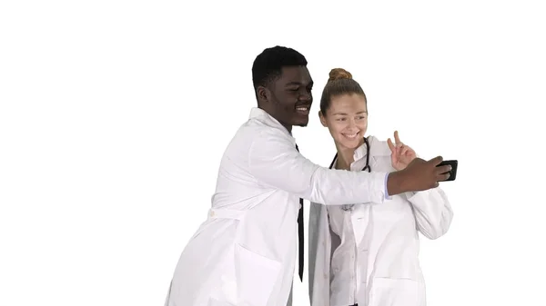 Dois médicos estão fazendo selfie usando um smartphone e sorrindo no fundo branco . — Fotografia de Stock