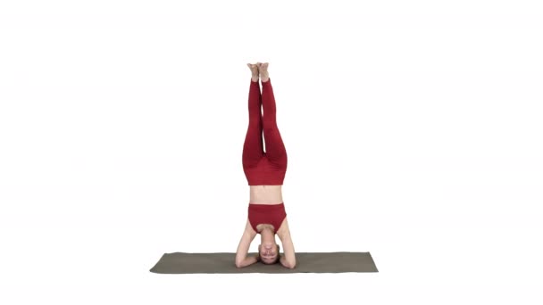 Hermosa joven haciendo yoga ejercicio variación de apoyada cabecera, garuda salamba sirsasana con piernas cruzadas sobre fondo blanco. — Vídeos de Stock