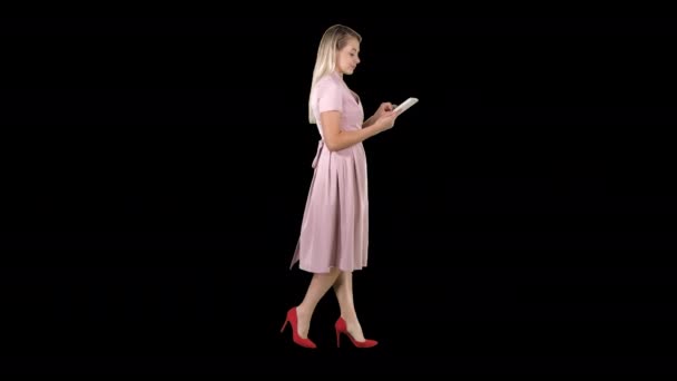 Blond i rosa klänning promenader och använda tablett, Alpha Channel — Stockvideo