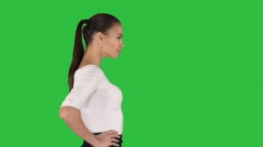 Şık kıyafet yürüyüş güzel genç kadın, bir yeşil ekran, Chroma Key kalçalarına üzerinde ellerimi.