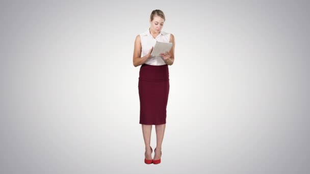 Atractiva mujer de negocios usando una tableta digital mientras está de pie en el fondo del gradiente. — Vídeos de Stock