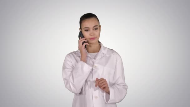 Усміхнена жінка-лікар по телефону розмовляє під час ходьби на градієнтному фоні . — стокове відео