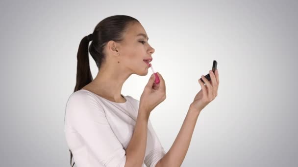 Mooie jonge vrouw zetten op lippenstift op gradiënt achtergrond. — Stockvideo