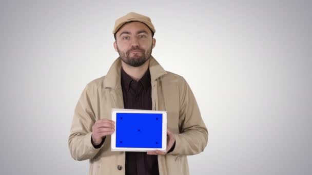 Uomo in trincea che cammina e tiene tablet con mockup schermo blu che presenta qualcosa su sfondo sfumato. — Video Stock