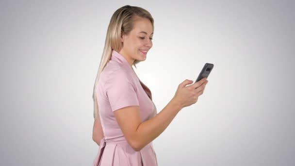 Mulher feliz selecionando conteúdo on-line em um telefone inteligente no fundo gradiente . — Vídeo de Stock