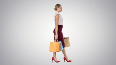 Her elde kağıt poşet tutan ve arka planda yürüyen uzun boylu mutlu bir kadın..