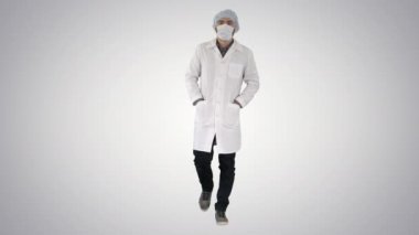 Degrade arka plan üzerinde ameliyat maskesi giyen genç erkek doktor yürüyüş.