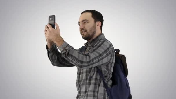 Atractivo turista joven con mochila caminando y el uso de teléfono móvil en el fondo gradiente . — Vídeos de Stock