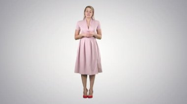 Pembe elbiseli sarışın kadın, arka planda kamerayla konuşuyor..