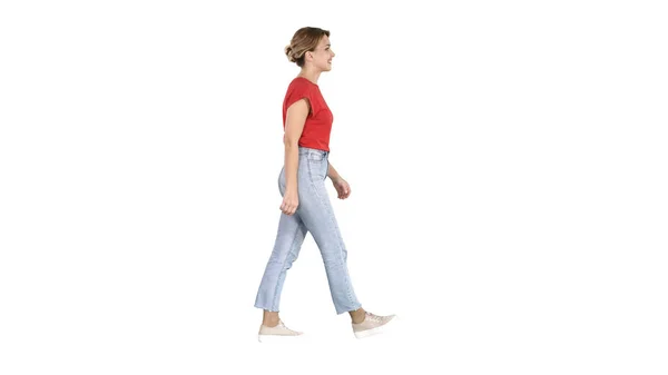 Mujer en camiseta roja, jeans y zapatillas de deporte caminando sobre fondo blanco . —  Fotos de Stock