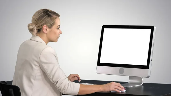 Młoda kobieta pracuje w biurze, siedząc przy biurku, patrząc na monitor na tło gradientowe. — Zdjęcie stockowe