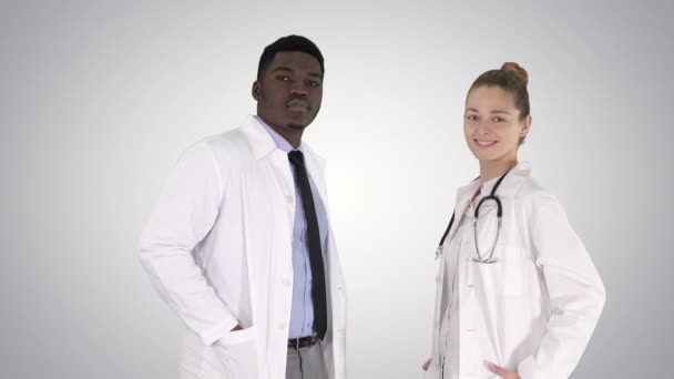 Deux médecins caucasiens et afro-américains souriants regardant à la caméra sur fond de gradient. — Video