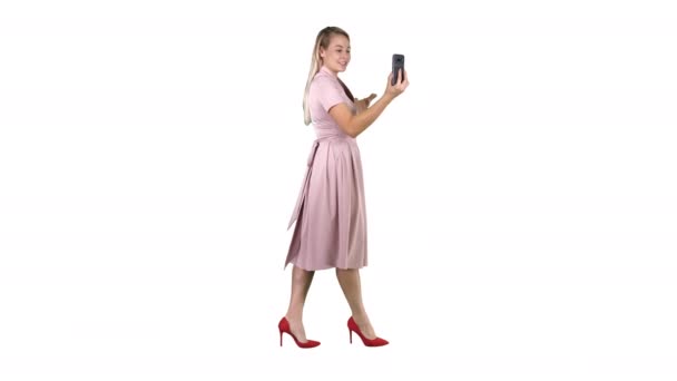 Jeune femme en tenue rose en utilisant le blog vidéo d'enregistrement de téléphone intelligent tout en marchant sur fond blanc . — Video