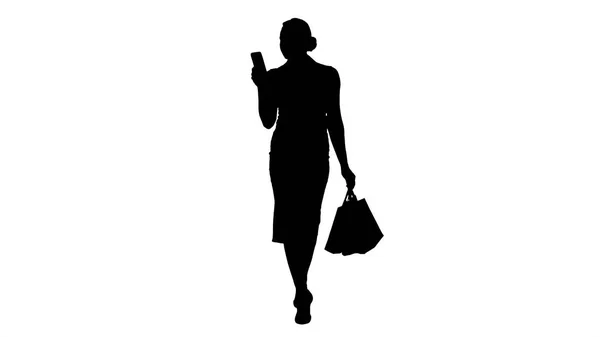 Silhouet van mooie aantrekkelijke vrouwen op zoek in smartphone en boodschappentassen te houden tijdens het lopen. — Stockfoto