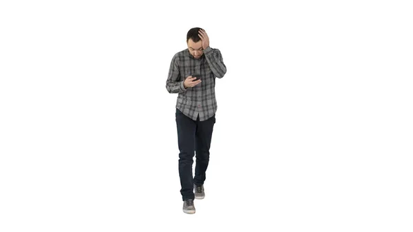 Shoked young man holding phone and reading message when walking on white background. — Stock Photo, Image