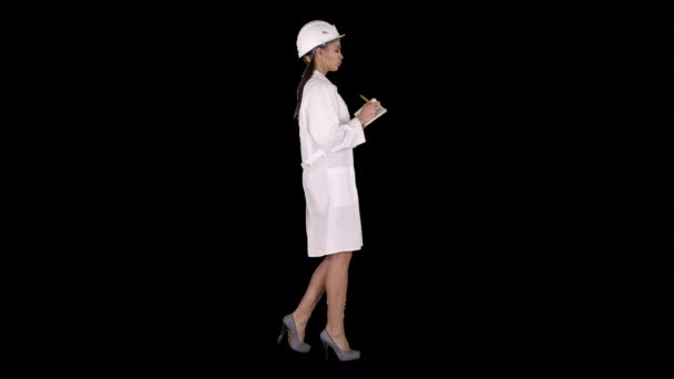 Vrouw ingenieur met helm houdt pen en checklist zet iets neer tijdens het lopen, Alpha Channel — Stockvideo