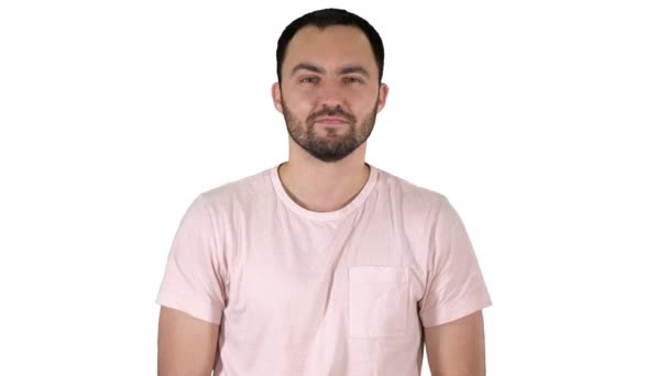 Молодий щасливий чоловік у футболці посміхається на камеру і ходить на білому тлі . — стокове відео