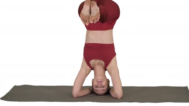 Hermosa joven haciendo yoga ejercicio variación de apoyada cabecera, garuda salamba sirsasana con piernas cruzadas sobre fondo blanco. — Vídeo de stock