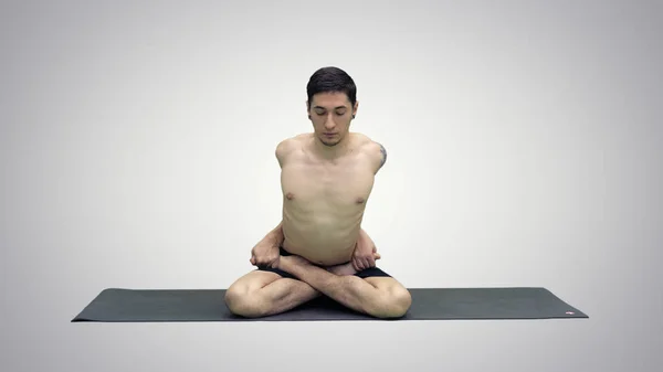 Sportliche schöne junge Mann praktiziert Yoga, sitzt im Schneidersitz in adho mukha padmasana, beugt sich nach vorne in Variation der Lotus-Pose auf Steigungsuntergrund. — Stockfoto