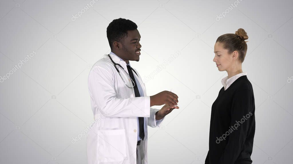 Male doctor offers medication to young woman on gradient background.