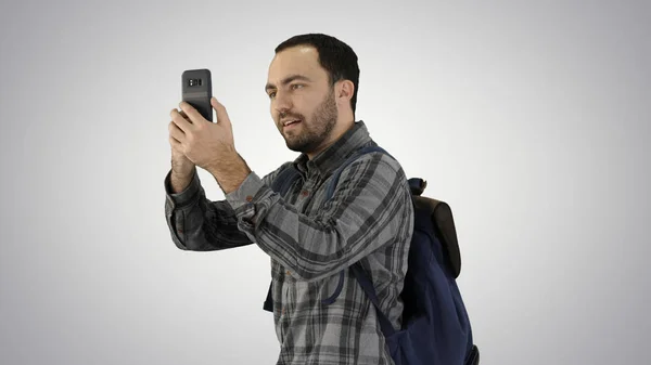 Attractive young tourist with backpack walking and using mobile phone on gradient background. — Stock Photo, Image