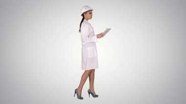 Degrade arka plan nesnelerini çevreleyen bakarak tablet ile yürüyen genç bir kadın mühendis.