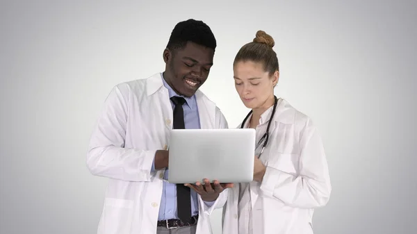 Medical staff working in front of a grey laptop while standing on gradient background.