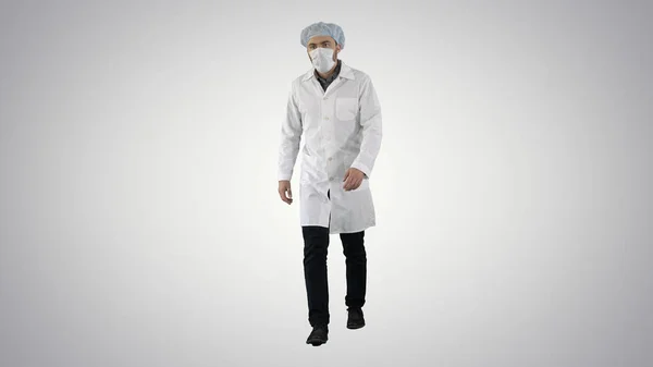 Chodzenie młody lekarz w masce i czapce medycznej na tle gradientu. — Zdjęcie stockowe