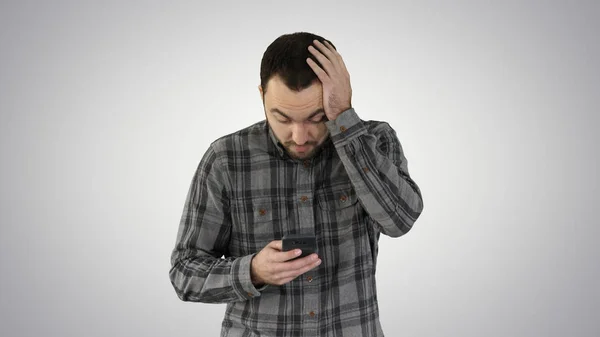 Stressed young man shocked surprised, horrified and disturbed, by what he sees on his cell phone on gradient background. — Stock Photo, Image