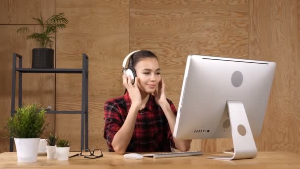 Chica alegre en la oficina escuchando música en los auriculares . — Vídeos de Stock