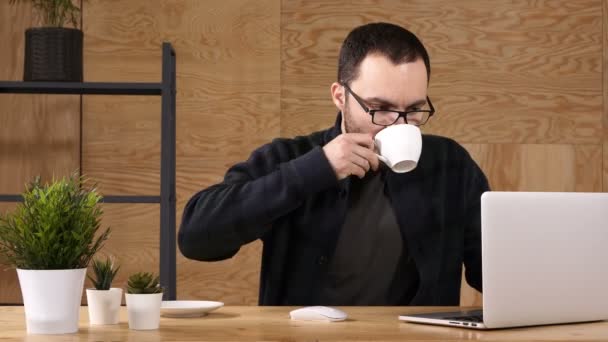 Ung bearded man dricker kaffe eller te medan du arbetar på laptop. — Stockvideo