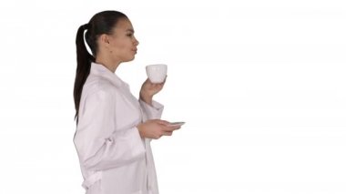 Genç hemşire beyaz arka planda yürürken kahve ya da çay içerek rahatlıyor..