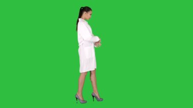 Genç kadın eczacı beyaz elbise ceket üniformalı bir yeşil ekranda Chroma Key yürüyüş.