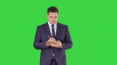Bir yeşil ekran, chroma key yürürken yakışıklı deneyimli Yöneticisi Notebook fikirlerini yazma.