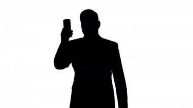 Siluet Genç işadamı yürürken iş ortağını aramak için akıllı telefonu kullanıyor.