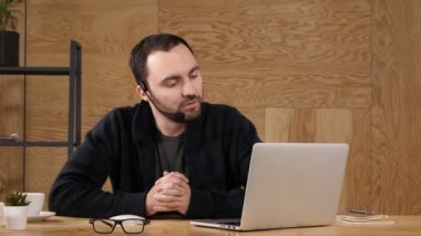 parlak bir ofiste bilgisayar kullanarak kulaklık rahat genç adamla gülümseyen.