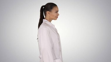 Beyaz bir elbise içinde doktor Şevval Özçelik Güzellik degrade arka plan üzerinde yürüyor.