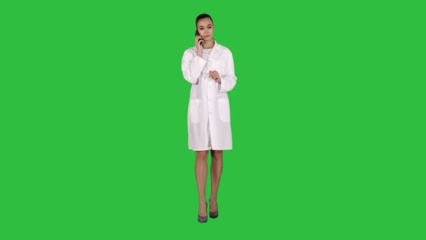 Docteur féminin de sourire sur le téléphone parlant tout en marchant sur un écran vert, clé de Chroma. — Video