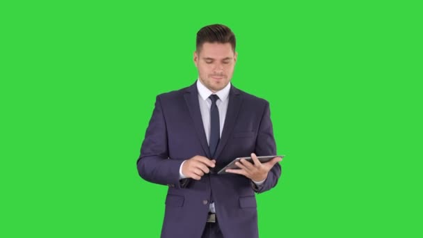 Businessman walking and swiping pages on his tablet computer and looking to camera presenting something on a Green Screen, Chroma Key. — Stock Video