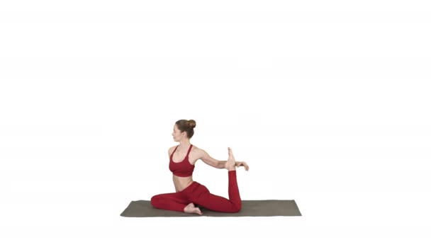 Vacker ung kvinna bär röda sportkläder gör yoga eller pilates utöva en fyrbent King Pigeon pose, Eka Pada Rajakapotasana på vit bakgrund. — Stockvideo